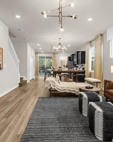 Open-plan living room with wood flooring, brown leather sofa, dark accent wall with TV, and kitchen visible in background
